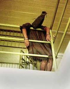 Along an Abu Ghraib prison walkway, a hooded detainee seems to have collapsed with his wrists handcuffed to the railings.